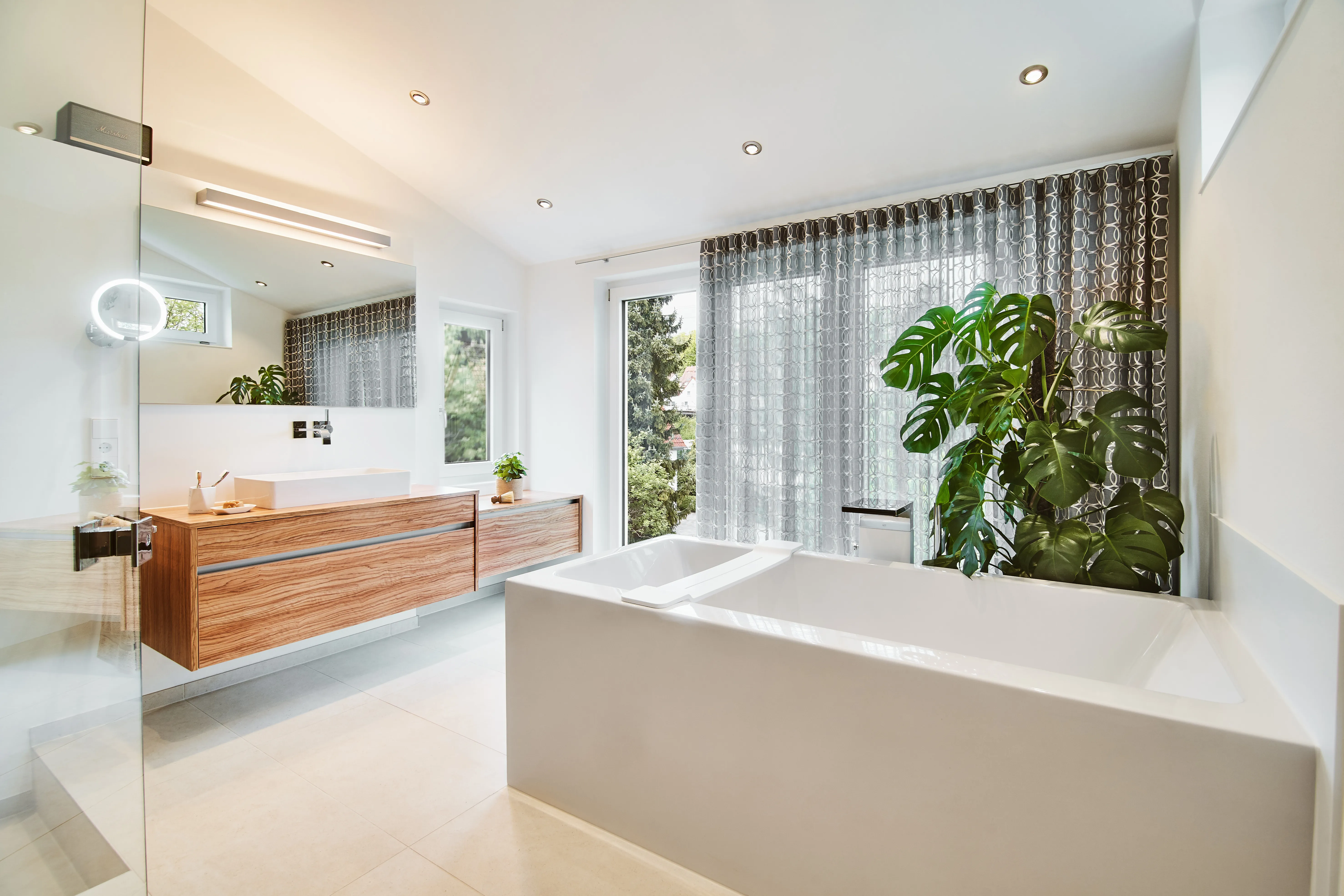 Helles Badezimmer mit freistehender Badewanne, Holzwaschtisch und großen Fensterflächen.
