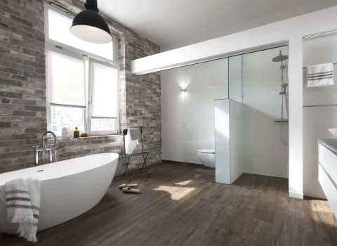 Freistehende ovale Badewanne in einem Badezimmer mit Ziegelwand und Holzfußboden.