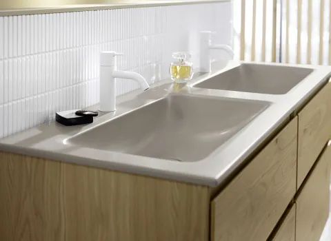 Doppelwaschtisch von Accura mit beigen Waschbecken und weißen, minimalistischen Armaturen. 