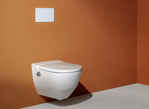 Ein modernes Badezimmer mit einer weißen, schwebenden Toilette vor einer warmen, orangefarbenen Wand.