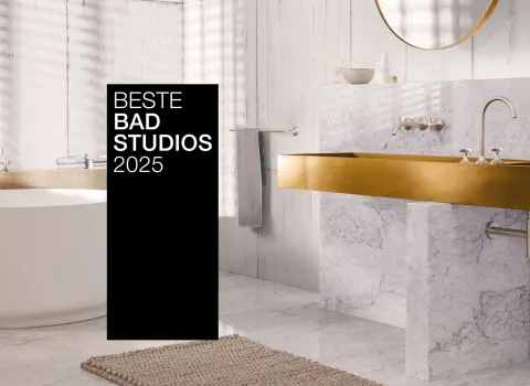 Ein stilvolles Bad mit goldenen Armaturen, Marmorwaschtisch und freistehender Badewanne. Ein schwarzer Banner mit "Beste Badstudios 2025" ist prominent im Bild.