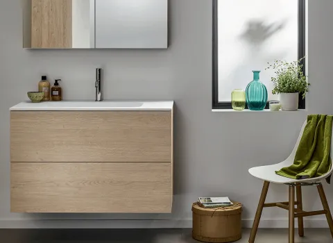 Modernes Stocco Badmöbel mit heller Holzfront, weißem Waschtisch und wohnlichen Accessoires am Fenster.
