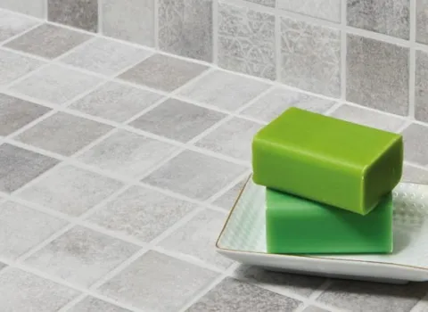 Seifenschale zwei grünen Seifen-Stücken auf einem Waschtisch mit hellgrauen Mosaikfliesen.