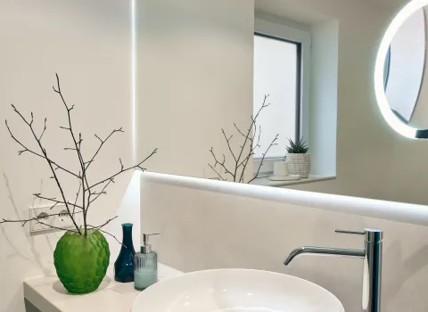 Rundes Aufsatzwaschbecken mit moderner Designarmatur und beleuchtetem Spiegel.