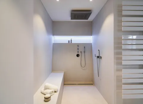 Begehbare Dusche mit Regendusche, Sitzbank und fugenarmer Wandgestaltung.