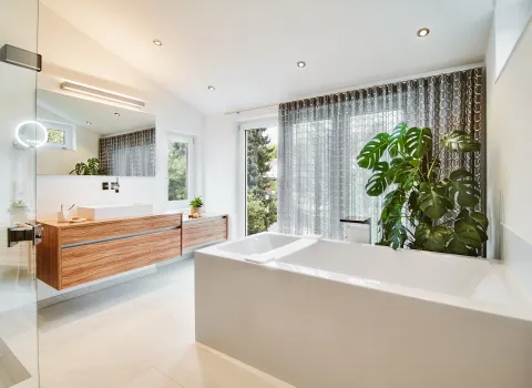 Helles Badezimmer mit freistehender Badewanne, Holzwaschtisch und großen Fensterflächen.