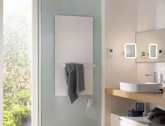 Ein minimalistischer weißer Heizkörper mit Handtuchhalter ist in einem hellen Badezimmer mit Aufsatzwaschbecken und Spiegeln angebracht.