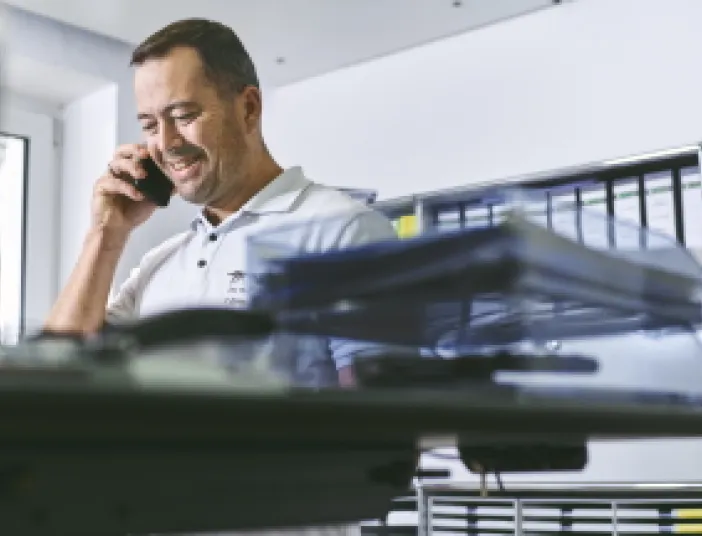 Ein lächelnder Projektleiter für Heizungsanlagen telefoniert in einem hellen Büroraum.