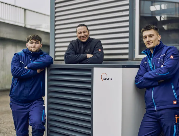 Drei Anlagenmechaniker SHK von bad und heizung posieren vor einer Waermepumpe von Solvis.