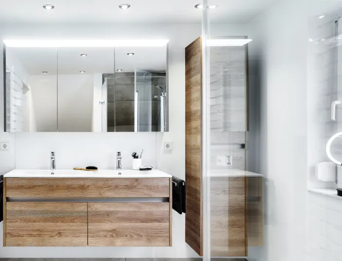 Modernes Badezimmer mit Doppelwaschtisch in Holzoptik und beleuchtetem Spiegelschrank.