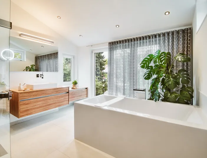 Helles Badezimmer mit freistehender Badewanne, Holzwaschtisch und großen Fensterflächen.