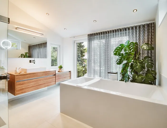 Helles Badezimmer mit freistehender Badewanne, Holzwaschtisch und großen Fensterflächen.