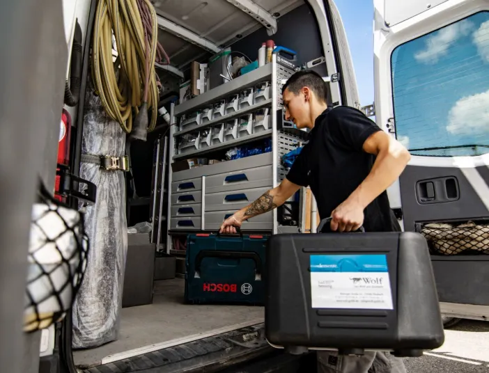 Ein Anlagenmechaniker Sanitär belädt einen Sprinter mit Werkzeugkisten.