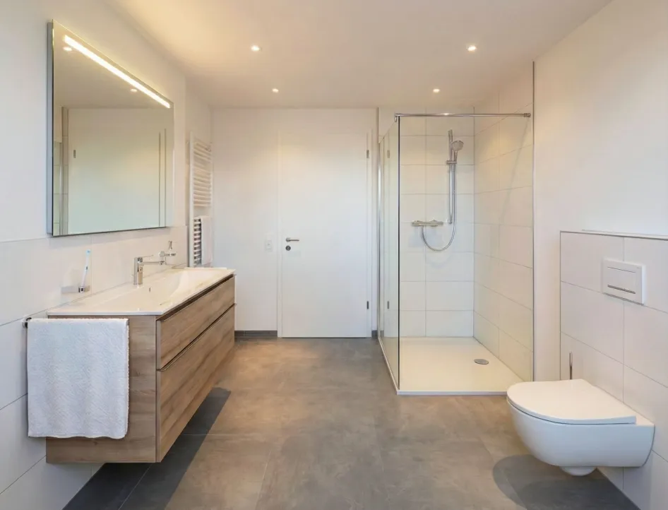 Fotorealistischer Planungsentwurf eines geräumigen Economy-Bades mit Glasdusche, Holzwaschtisch und großem Spiegel. Dezente Ausstattung für einen schlichten, eleganten Look.